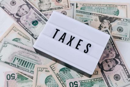 白板上的 "TAXES "标志覆盖着各种美元钞票,说明了与税收有关的概念,如 810 退税冻结程序及其对报税的影响。.
