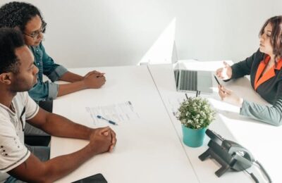 Couple consulting with tax professional about IRS offer in compromise to resolve tax debt, seated at desk with laptop and documents in professional office setting