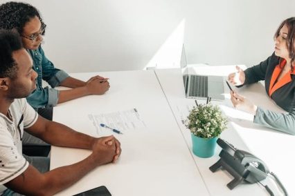 Couple consulting with tax professional about IRS offer in compromise to resolve tax debt, seated at desk with laptop and documents in professional office setting