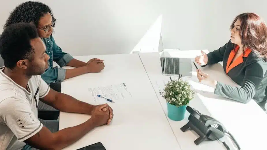 Couple consulting with tax professional about IRS offer in compromise to resolve tax debt, seated at desk with laptop and documents in professional office setting