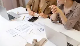 Two people review chart of accounts paperwork with a calculator nearby