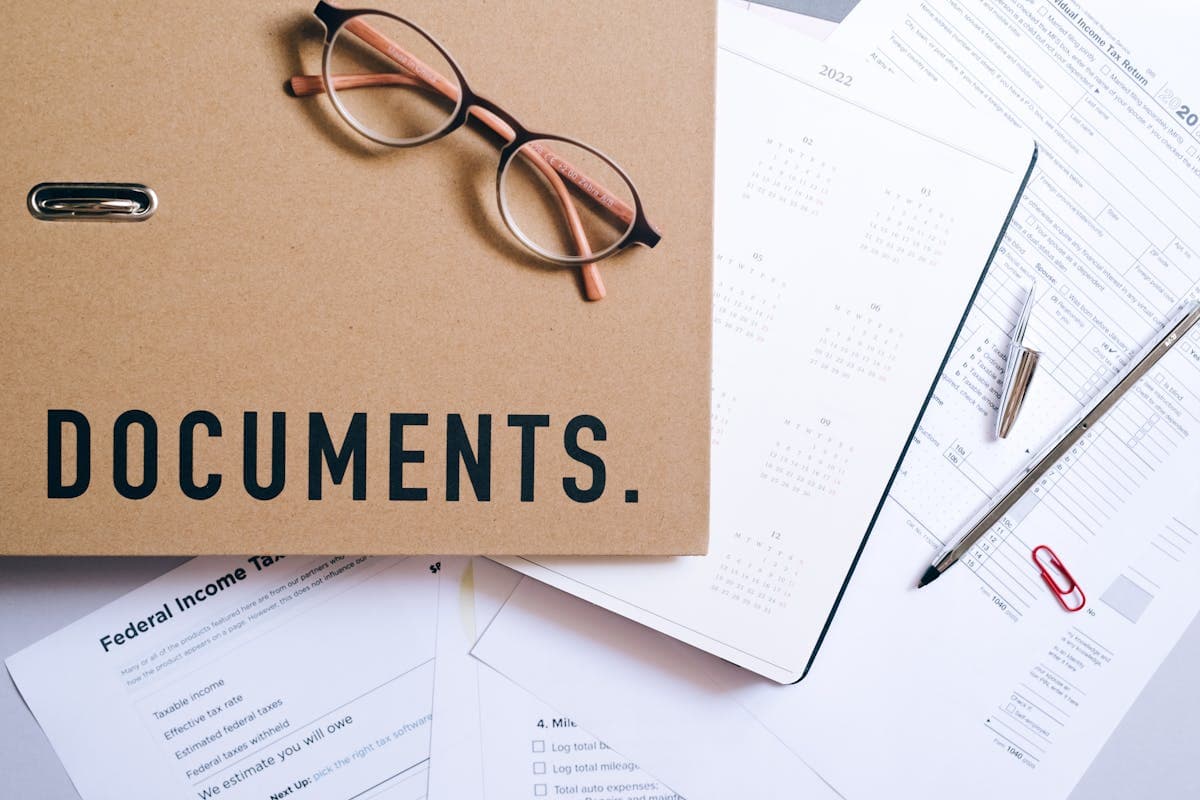 A set of tax-related documents, including federal income tax forms, a calendar, a folder labeled 'Documents,' and a pair of glasses. This image illustrates the process of tax filing, relevant to electric vehicle tax credits and other financial records.