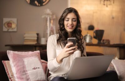 Woman smiling while checking her FICA tax refund on smartphone, sitting with laptop at home, illustrating the satisfaction of reclaiming hard-earned cash.