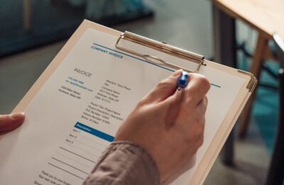 Close-up of hands filling out a company invoice form on a clipboard, potentially related to Florida taxable services documentation and billing practices.