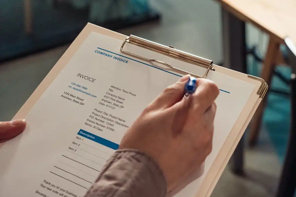 Close-up of hands filling out a company invoice form on a clipboard, potentially related to Florida taxable services documentation and billing practices.