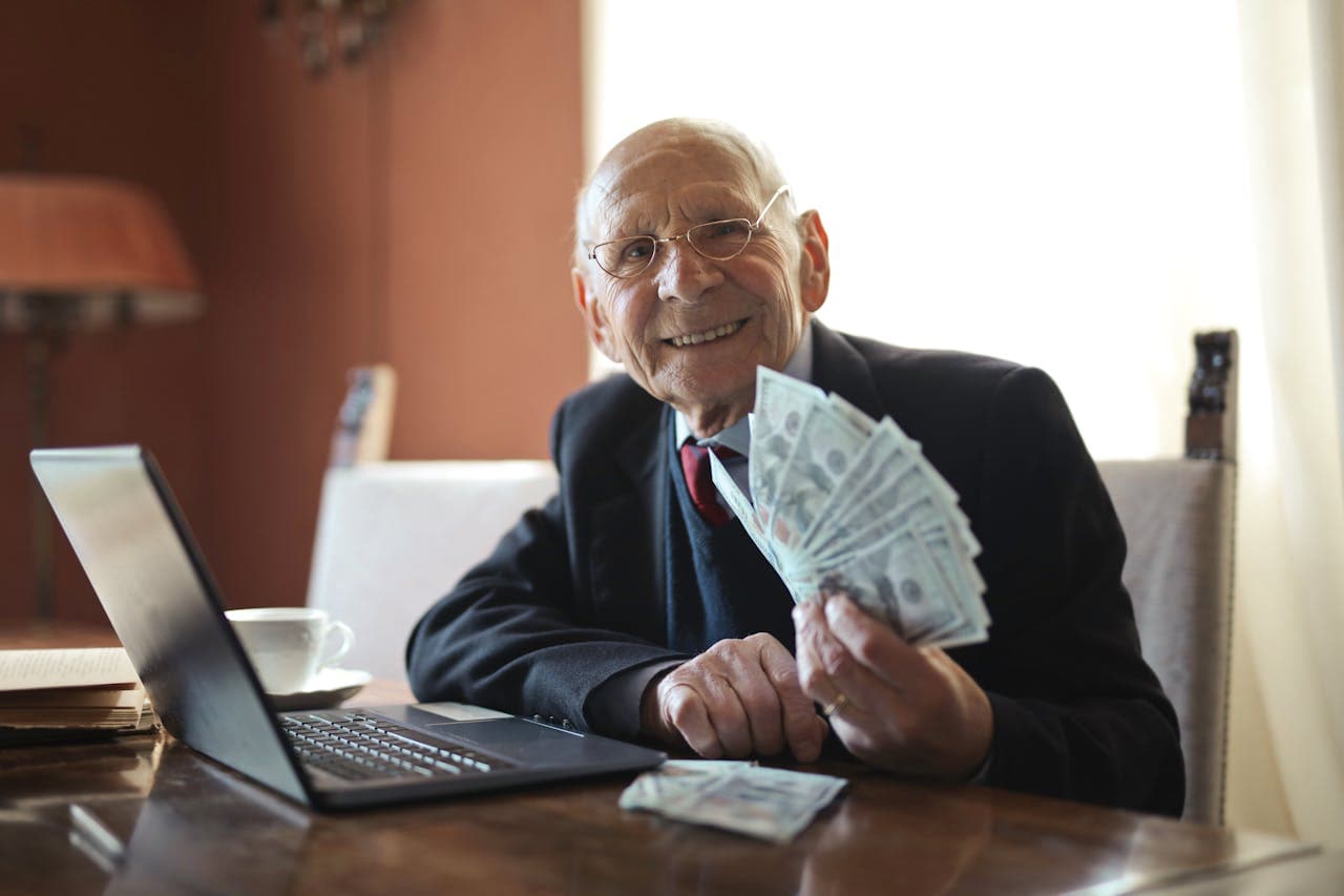 Un hombre de negocios sonríe mientras sostiene dinero en efectivo, demostrando el éxito potencial de reclamar la propiedad no reclamada de Florida, con un ordenador portátil cerca.