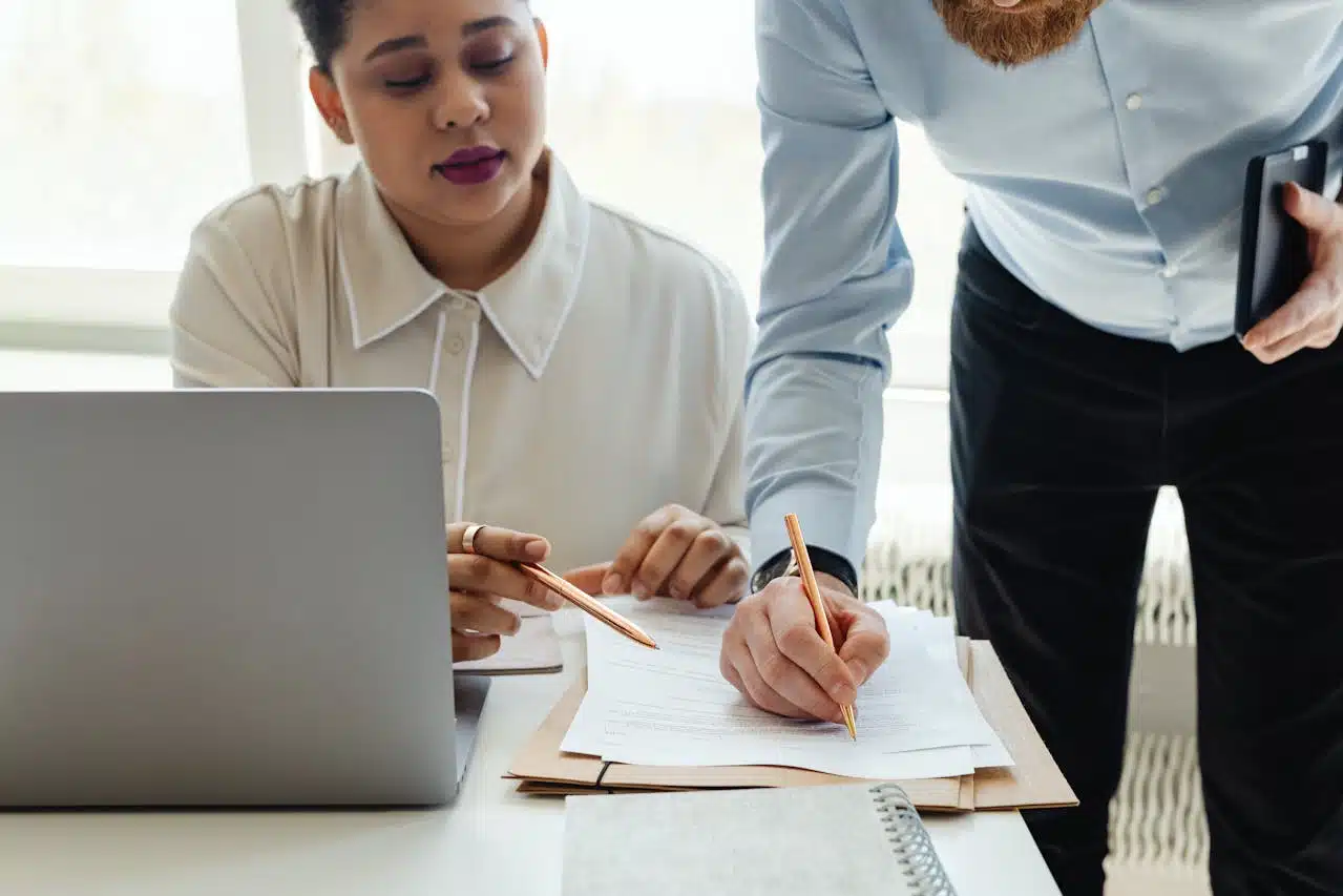 Two professionals reviewing Form 843 instructions at a desk, with a woman in a white blouse seated at a laptop while her colleague stands beside her as they examine paperwork.