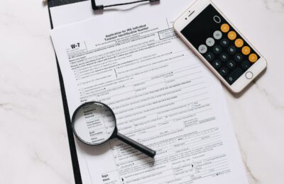 Form W-7 ITIN application on clipboard with magnifying glass and smartphone calculator, illustrating the process of applying for an Individual Taxpayer Identification Number