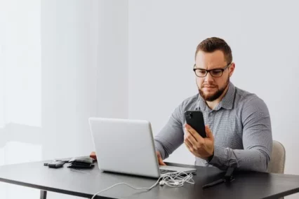 Man using a smartphone and laptop for ID.me identity verification.