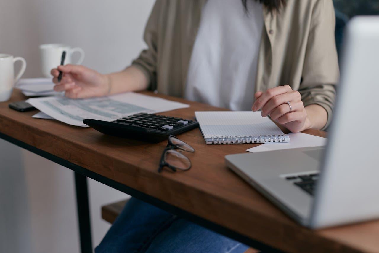 Person working on tax documents related to IRS Code 290, with calculator, notebook, and laptop on desk, illustrating the process of decoding and addressing tax issues.