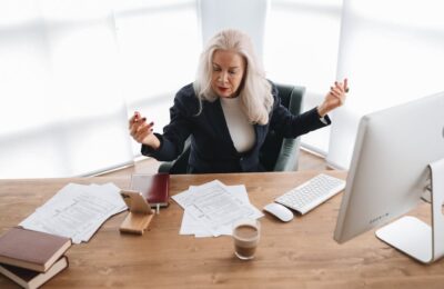 Woman expressing frustration while dealing with IRS Code 570 refund hold, surrounded by tax documents, computer, and paperwork on her desk, illustrating the stress of resolving tax issues.