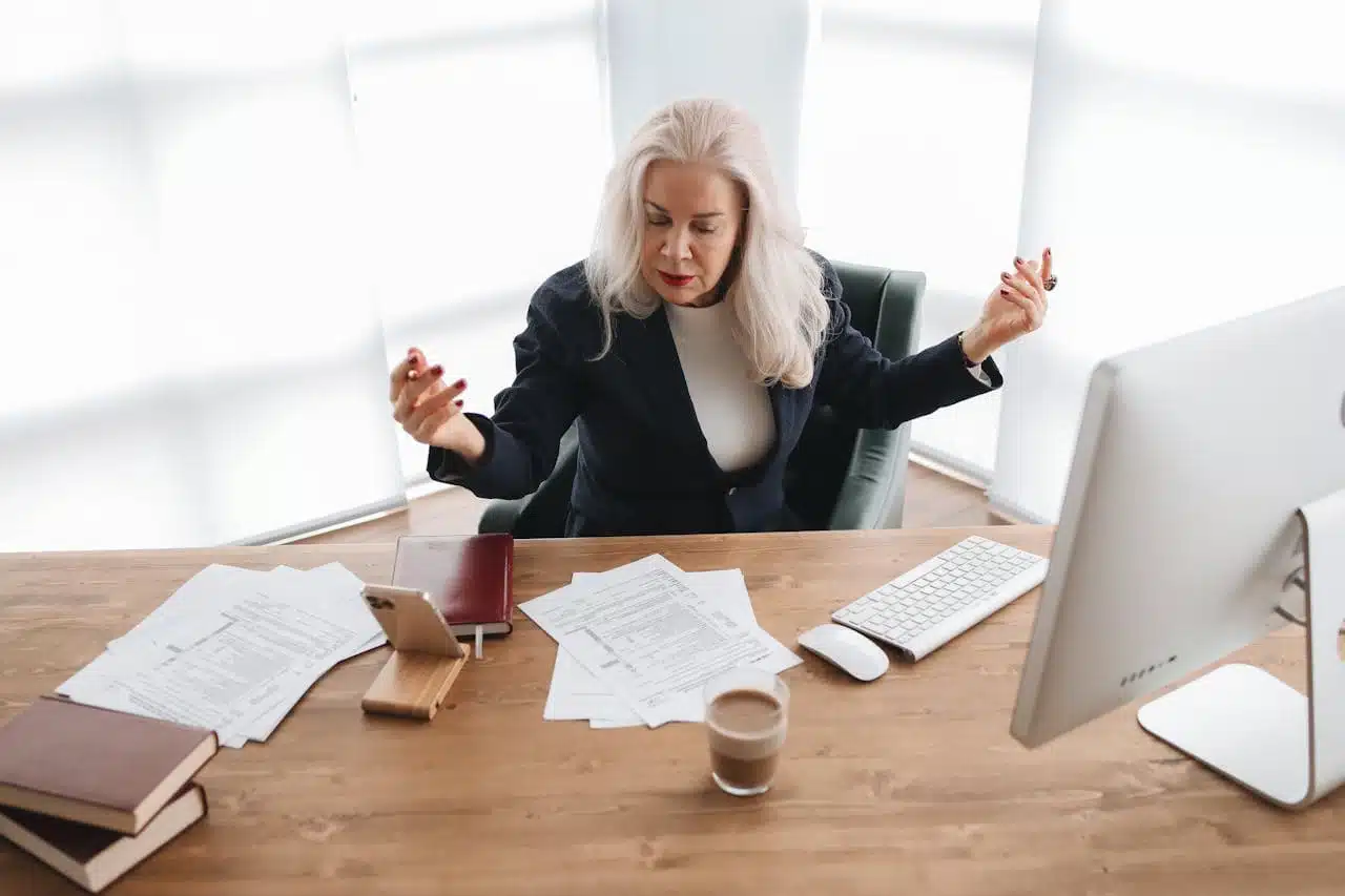 Woman expressing frustration while dealing with IRS Code 570 refund hold, surrounded by tax documents, computer, and paperwork on her desk, illustrating the stress of resolving tax issues.