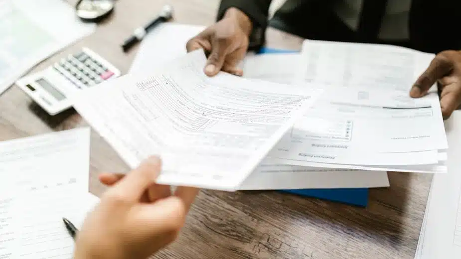 Hands reviewing financial transcripts on a wooden desk with calculator, potentially discussing IRS code 971 implications.