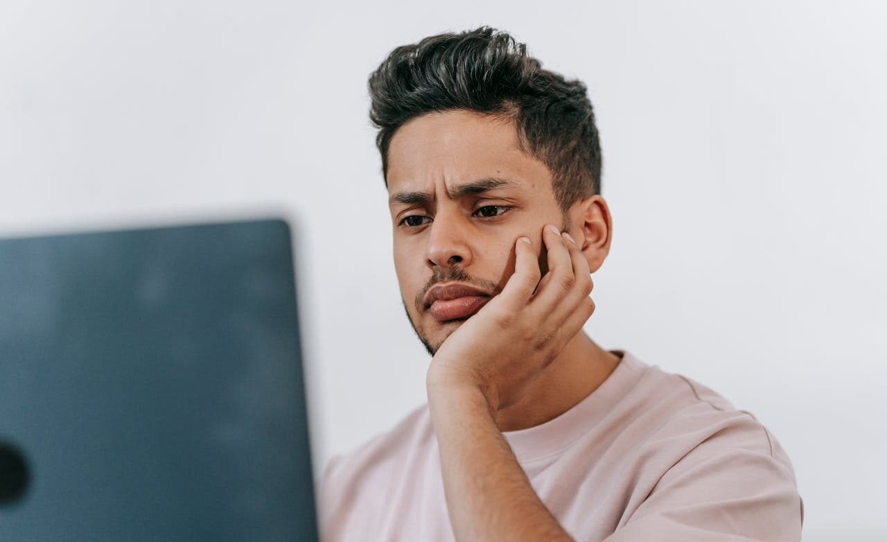 Man looking confused while using laptop, potentially struggling with IRS transcript codes tool, illustrating the complexity of interpreting tax documents.