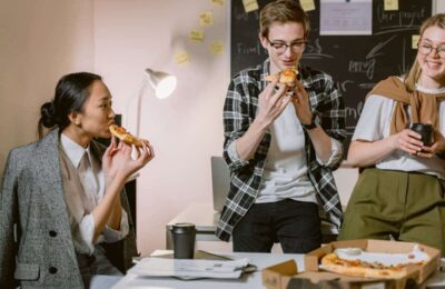 Coworkers sharing pizza in office, illustrating deductible meals and entertainment expenses in workplace settings