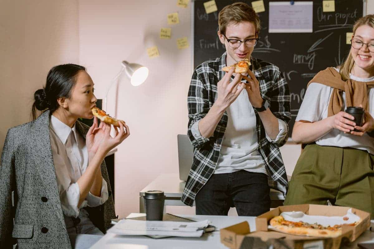 Coworkers sharing pizza in office, illustrating deductible meals and entertainment expenses in workplace settings