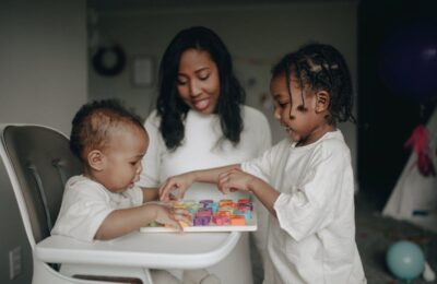 Two young children engaged in a colorful learning activity with alphabet blocks while a caregiver supervises, illustrating childcare scenarios relevant to nanny tax considerations.