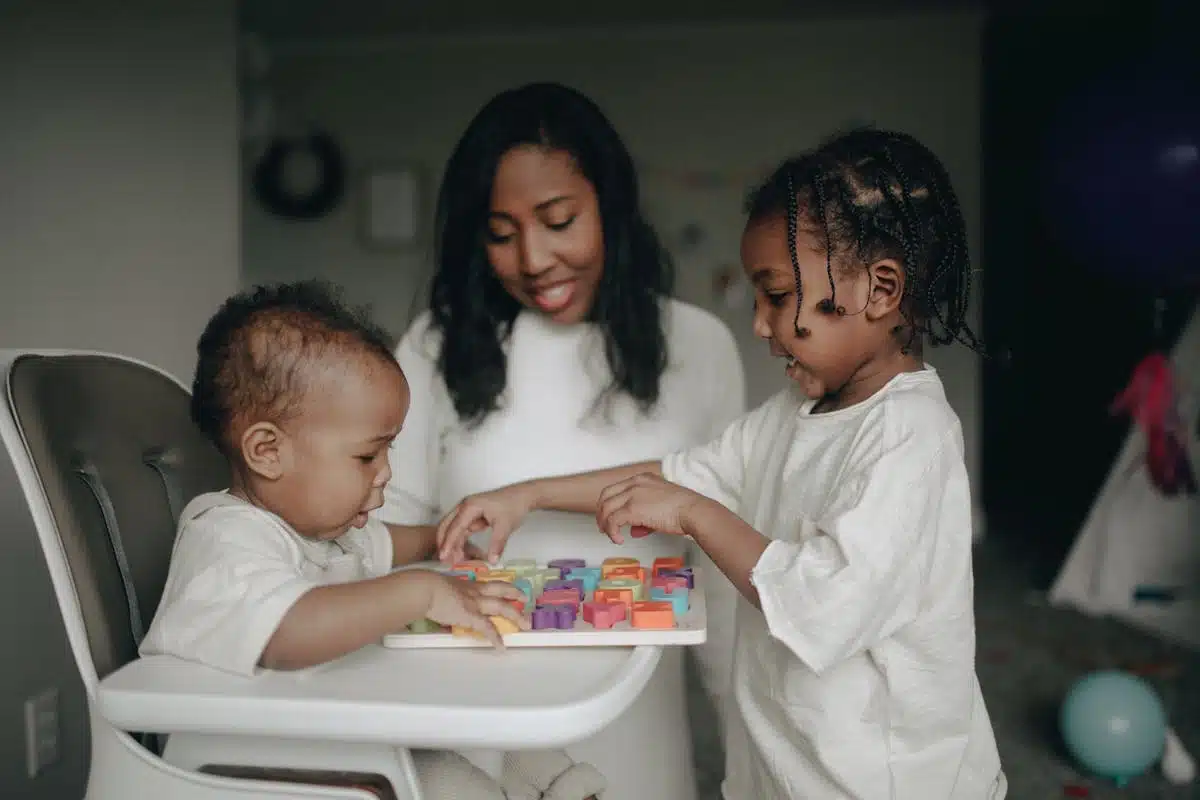 Two young children engaged in a colorful learning activity with alphabet blocks while a caregiver supervises, illustrating childcare scenarios relevant to nanny tax considerations.