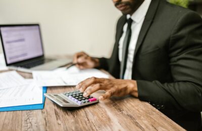 Tax professional in suit working on financial documents, using calculator and laptop, illustrating the pros and cons of hiring a tax professional for complex tax situations.