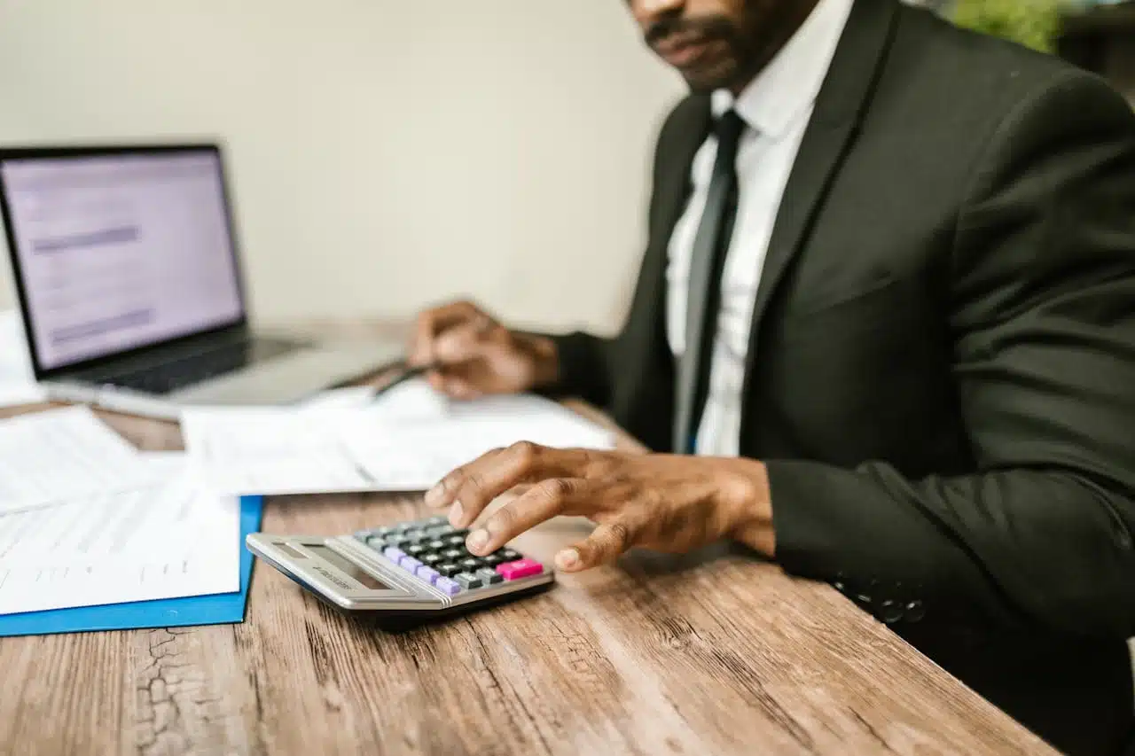 Tax professional in suit working on financial documents, using calculator and laptop, illustrating the pros and cons of hiring a tax professional for complex tax situations.