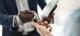 Close-up of hands exchanging keys, with one person in a business suit, suggesting a rental property transaction or management scenario related to rental property tax considerations.