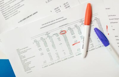 Financial statement with detailed expenses and Section 1231 assets analysis, featuring orange and blue pens for marking important figures on a consolidated report of functional expenses.