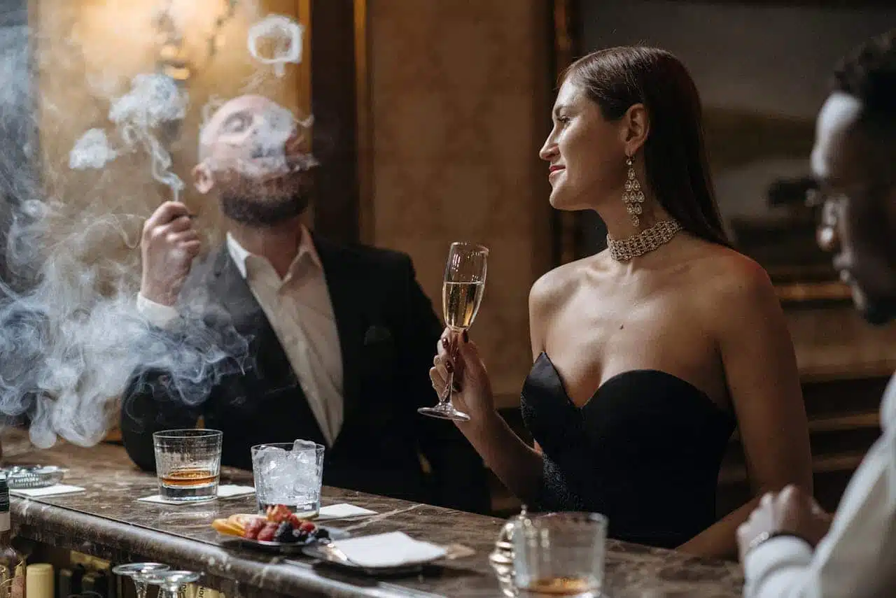 Elegant couple at upscale bar with champagne and cigar, illustrating luxury items subject to sin tax regulations in hospitality venues.