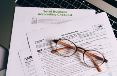 Small business tax forms including Schedule SE and 1040, with accounting checklist and glasses, highlighting common tax mistakes for entrepreneurs.