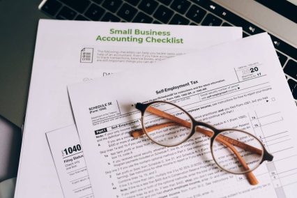 Formularios fiscales para pequeñas empresas, incluidos los anexos SE y 1040, con lista de verificación contable y gafas, en los que se destacan los errores fiscales más comunes que cometen los emprendedores.