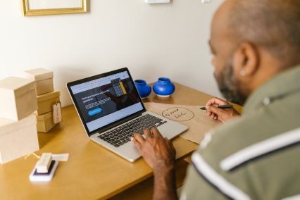 Hombre investigando cómo crear una sociedad de responsabilidad limitada en línea, usando una computadora portátil en un escritorio con un bloc de notas y material de oficina.