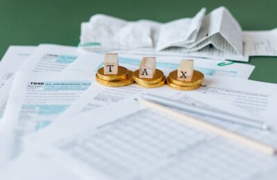 Tax preparation scene with wooden letters spelling 'TAX' on gold coins, atop IRS Form 1040 and other tax documents, illustrating concepts related to Tax Topic 203 on withholding of tax refund.