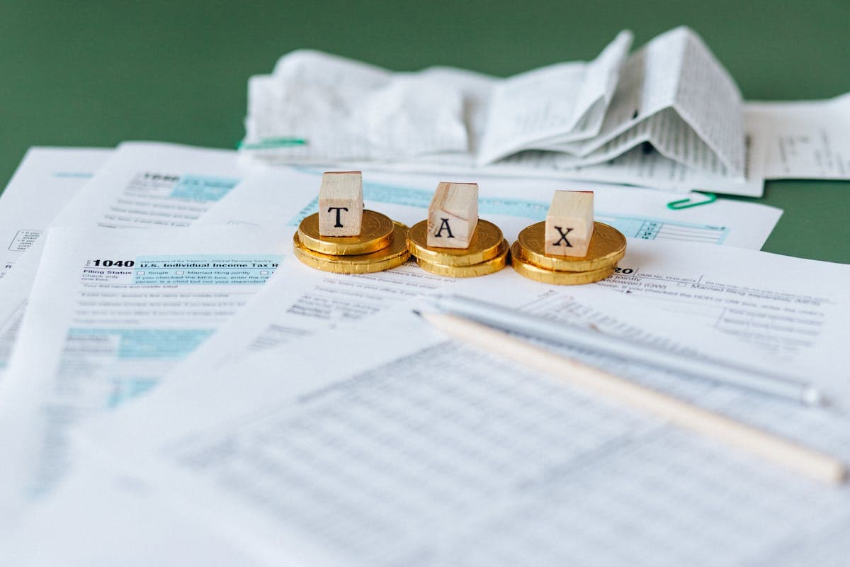 Tax preparation scene with wooden letters spelling 'TAX' on gold coins, atop IRS Form 1040 and other tax documents, illustrating concepts related to Tax Topic 203 on withholding of tax refund.